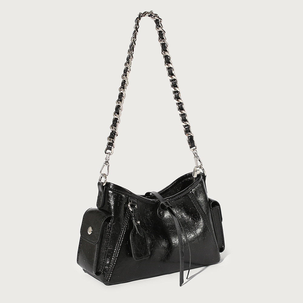 A glossy black crinkled vegan leather underarm bag with snap cargo side pockets, a chain strap, and a small luggage tag.