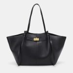 A large black vegan leather flared tote with long shoulder straps and a gold turn-lock on a slim horizontal strap.