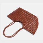 A black woven vegan leather shopper tote with braided handles and a cognac brown drawstring inner pouch. Additional product view 7.