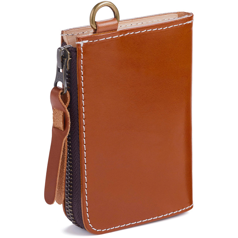A cognac vegetable-tanned leather zip wallet with white contrast stitching, a brass D-ring, and a leather zipper pull on a white background.