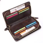 A black top-grain leather long wallet with a front flap, zip-around closure, and leather zipper pull on a white background. Additional product view 4.