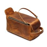 A vintage brown leather toiletry bag with dual zippers, a front flap pocket, side handle, and brass feet on a white background. Additional product view 2.