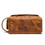 A vintage brown leather toiletry bag with dual zippers, a front flap pocket, side handle, and brass feet on a white background. Additional product view 3.