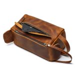 A vintage brown leather toiletry bag with dual zippers, a front flap pocket, side handle, and brass feet on a white background. Additional product view 4.