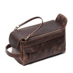 A vintage brown leather toiletry bag with dual zippers, a front flap pocket, side handle, and brass feet on a white background. Additional product view 6.